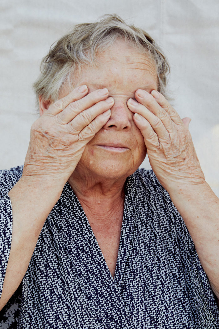 Portrait of grandmother, hands over eyes, tired